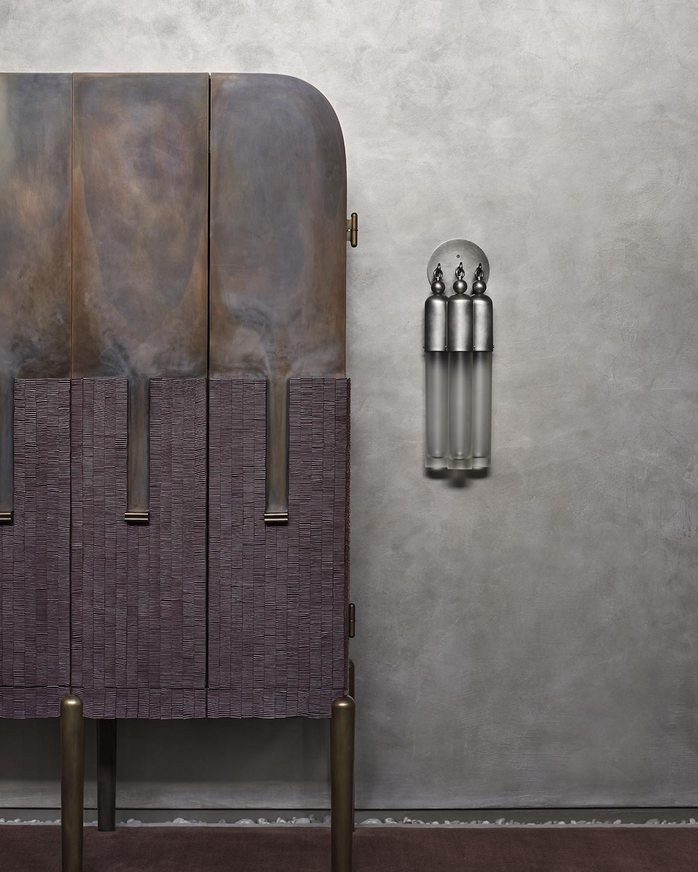 Minimalist wall sconce with three elongated frosted glass tubes and metallic decorative finials on a textured gray wall