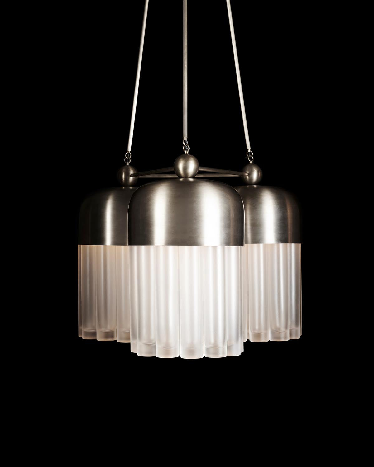 Modern pendant light fixture with brushed metal tops and frosted vertical glass tubes hanging against black background