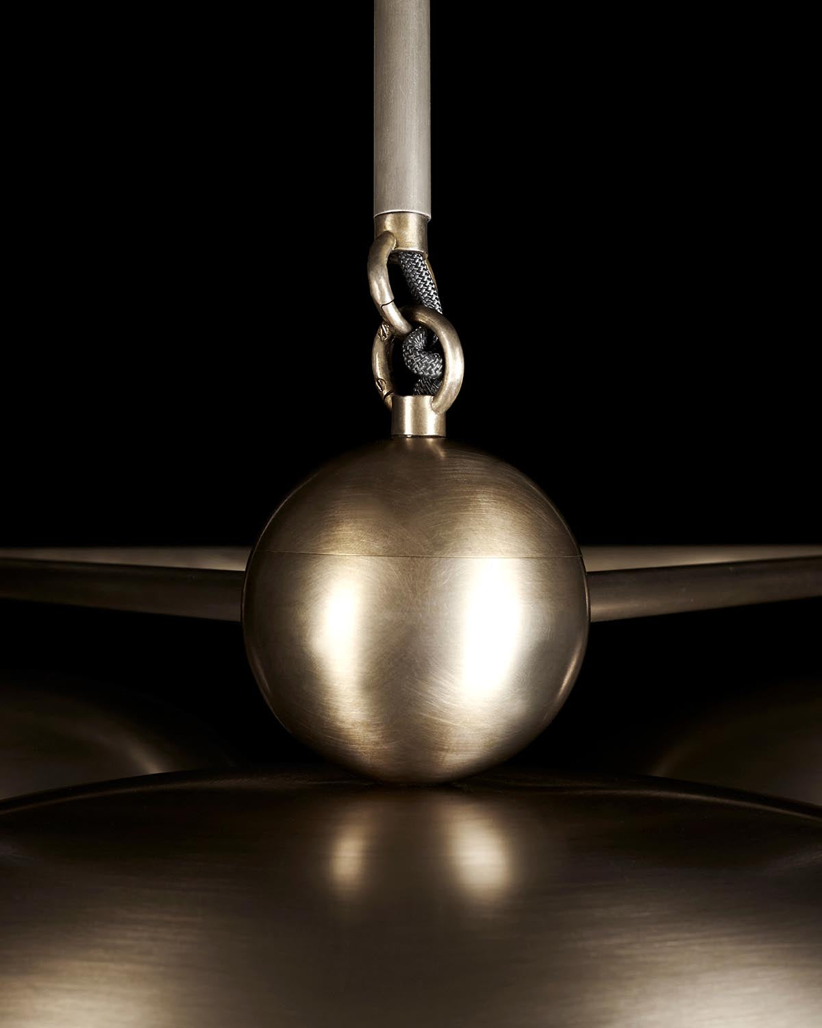 Close-up of a brushed metallic spherical pendant detail with textured cord and linked rings against a black background