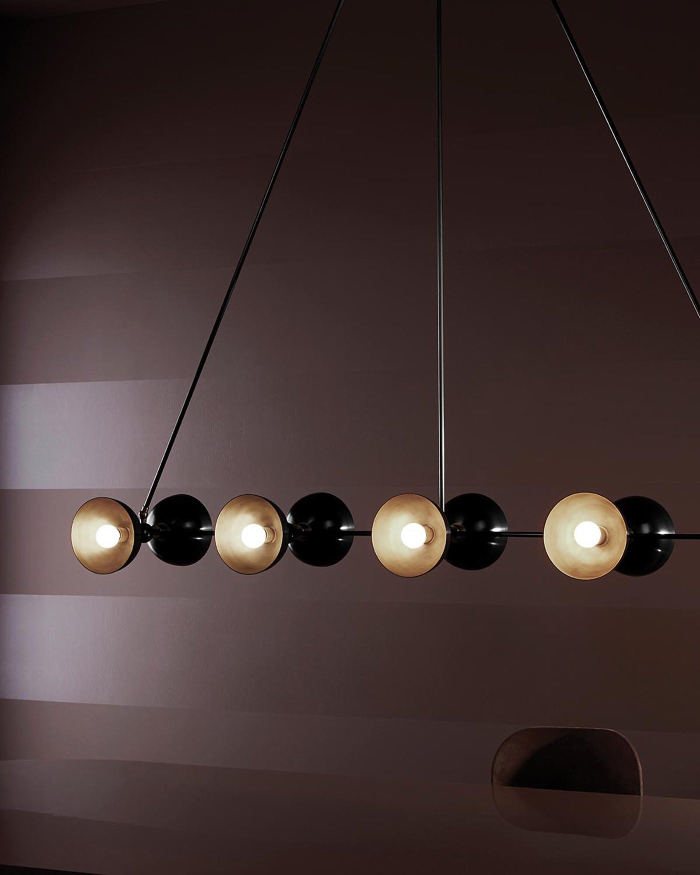 Linear pendant light fixture with alternating black and gold spherical shades suspended against a dark brown wall