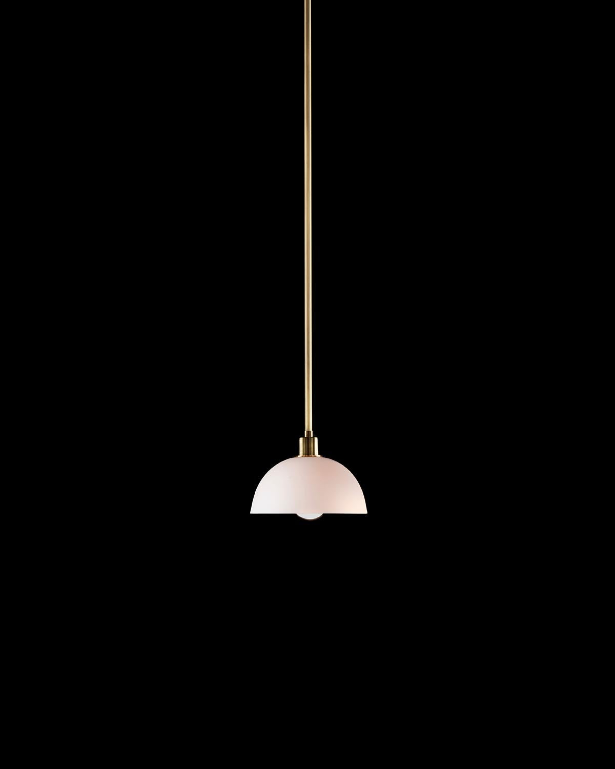 Minimalist pendant light with a matte white dome shade and slender brass rod suspension against a black background