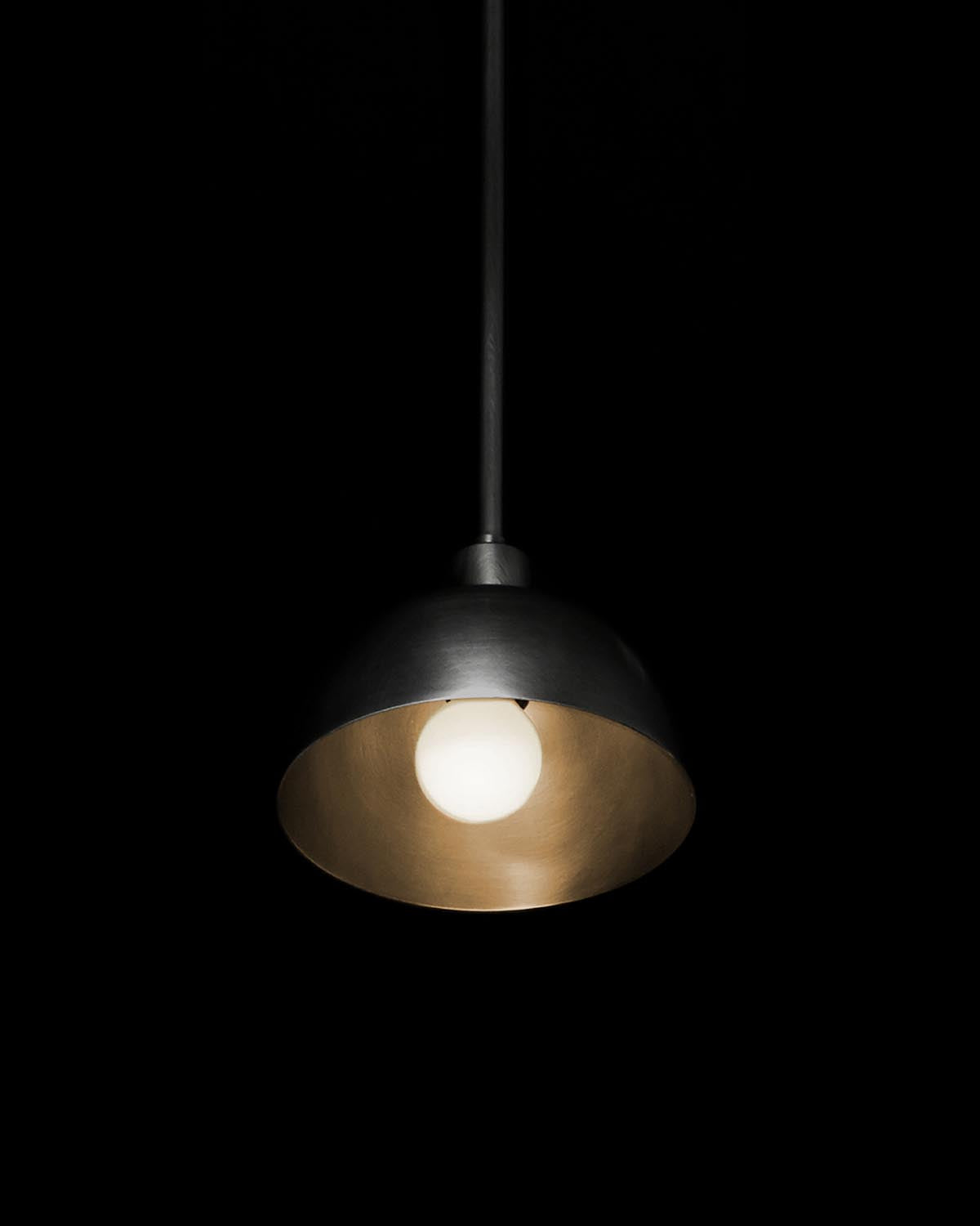 Single pendant light with dark metal dome shade and exposed bulb against a black background