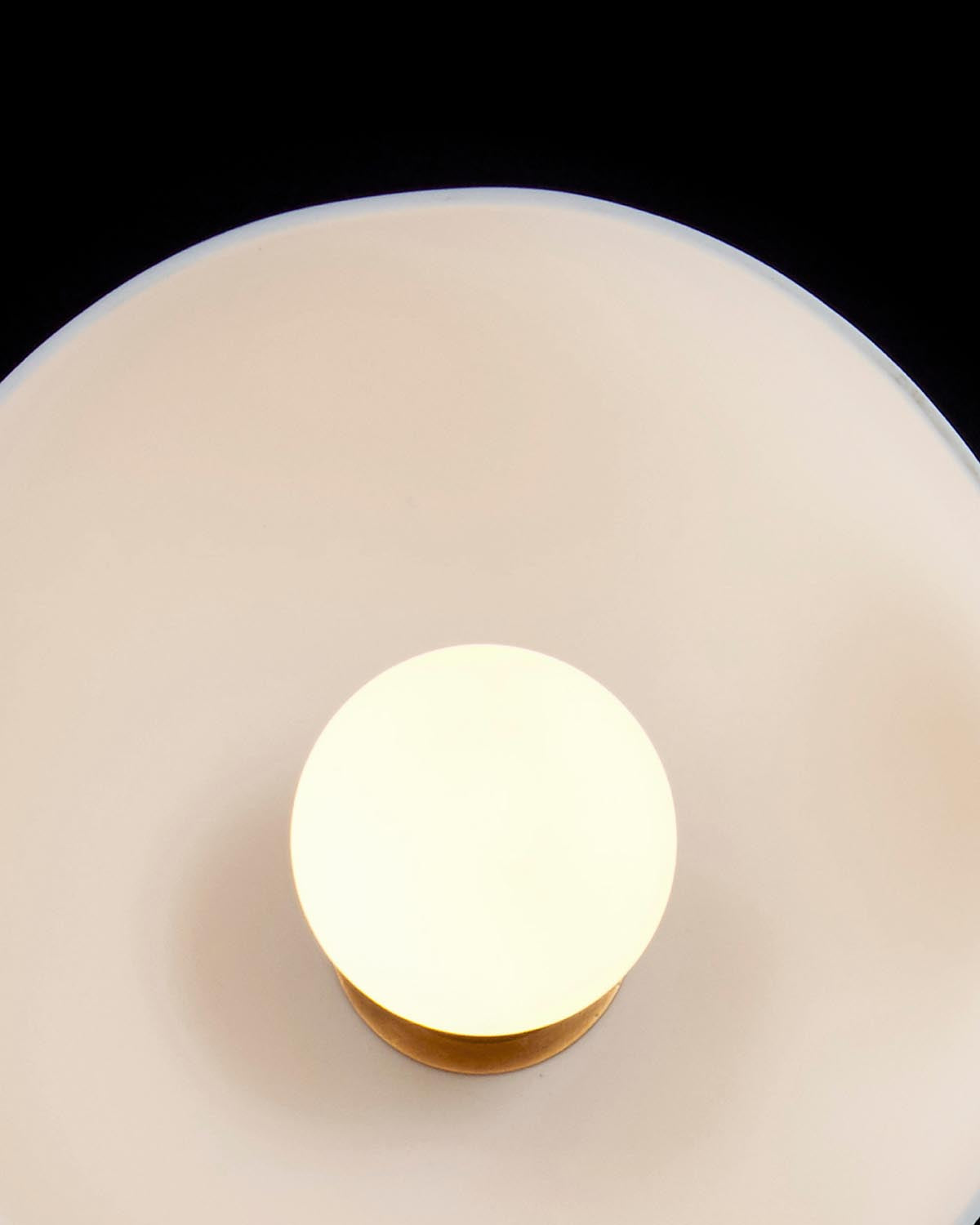 Overhead view of a round white surface with a glowing central orb on a brass base against a black background
