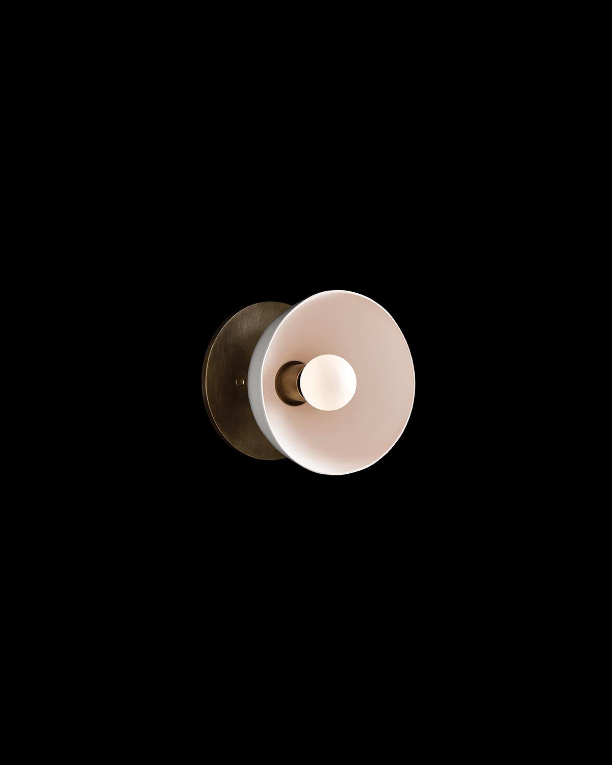 Wall-mounted light fixture with circular white shade and round brass base on black background