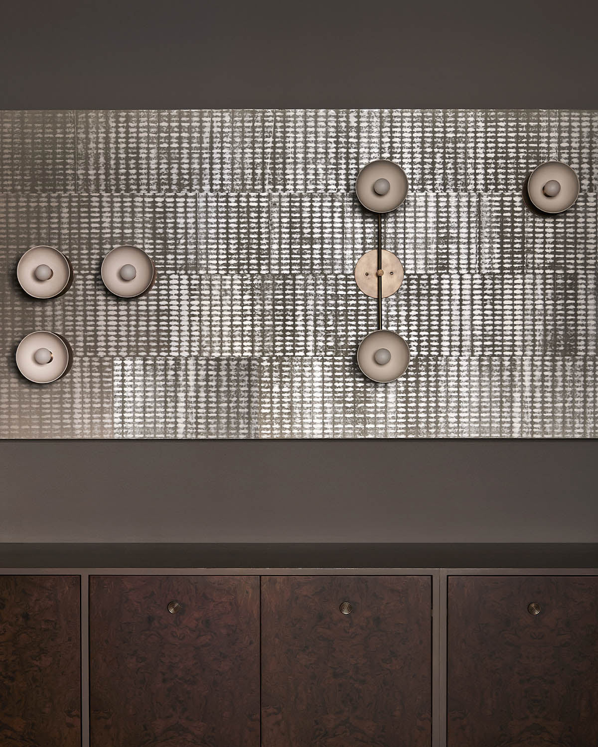 Rectangular textured panel with circular beige light fixtures mounted above dark wood cabinets against a taupe wall