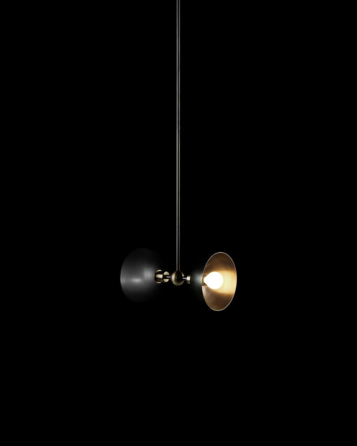 Close-up of a minimalist pendant light with a black and gold circular shade and exposed bulb against a black background
