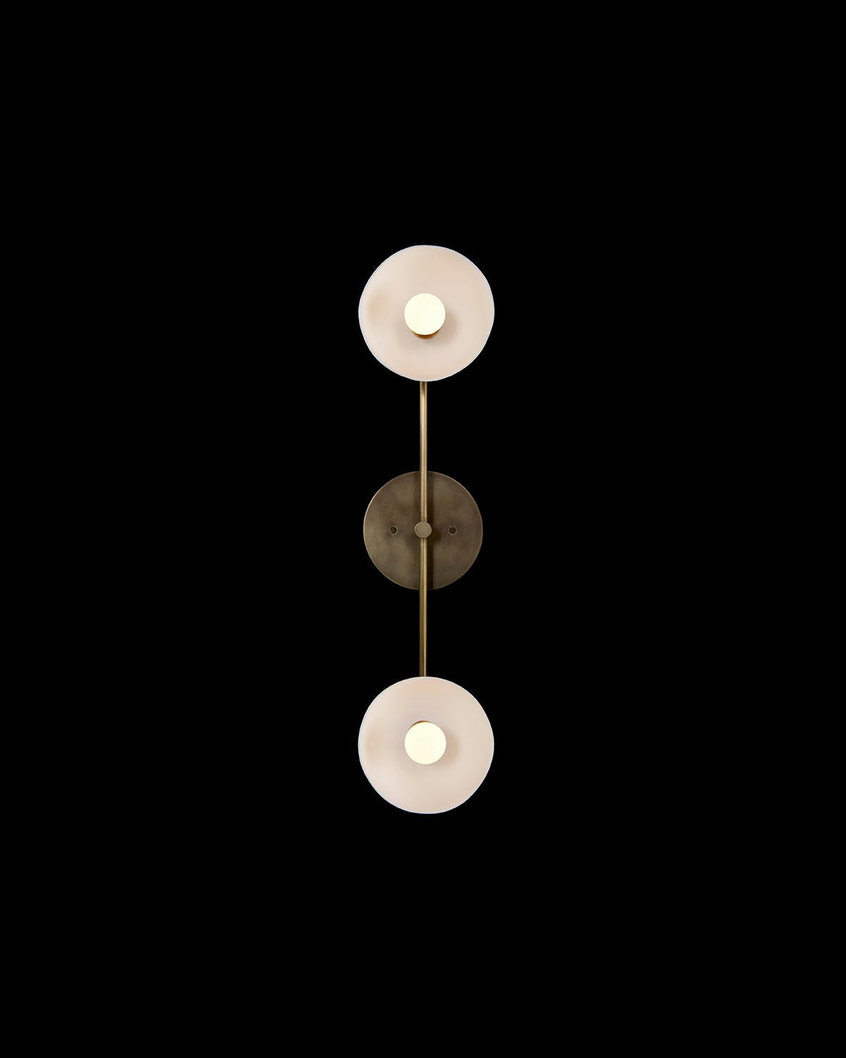 Minimalist double circular light fixture with frosted glass shades and brass accents on a black background