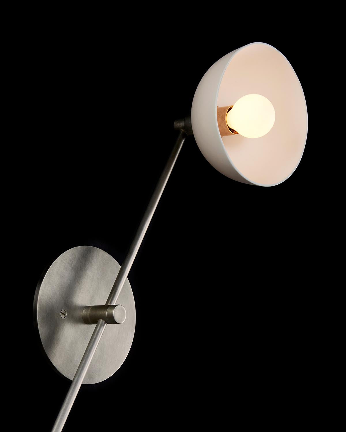 Minimalist wall lamp with angled metal arm and white conical shade illuminating a round light bulb against black background