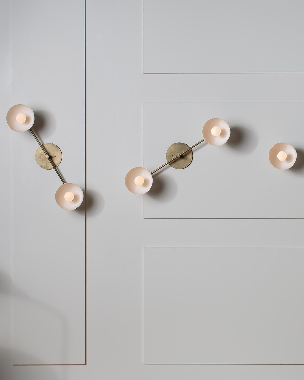 Two modern brass wall sconces with three frosted glass globe lights each mounted on a white paneled wall