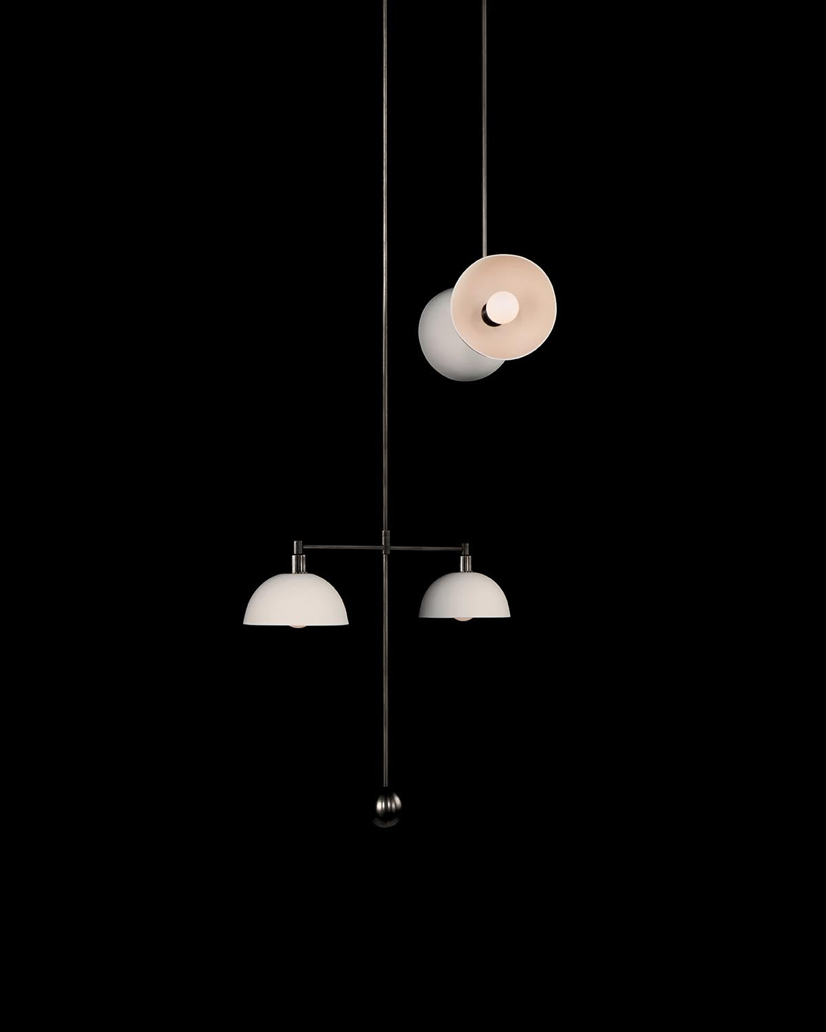Minimalist hanging mobile light fixture with two white dome shades and a circular shade suspended on thin black rods against black background