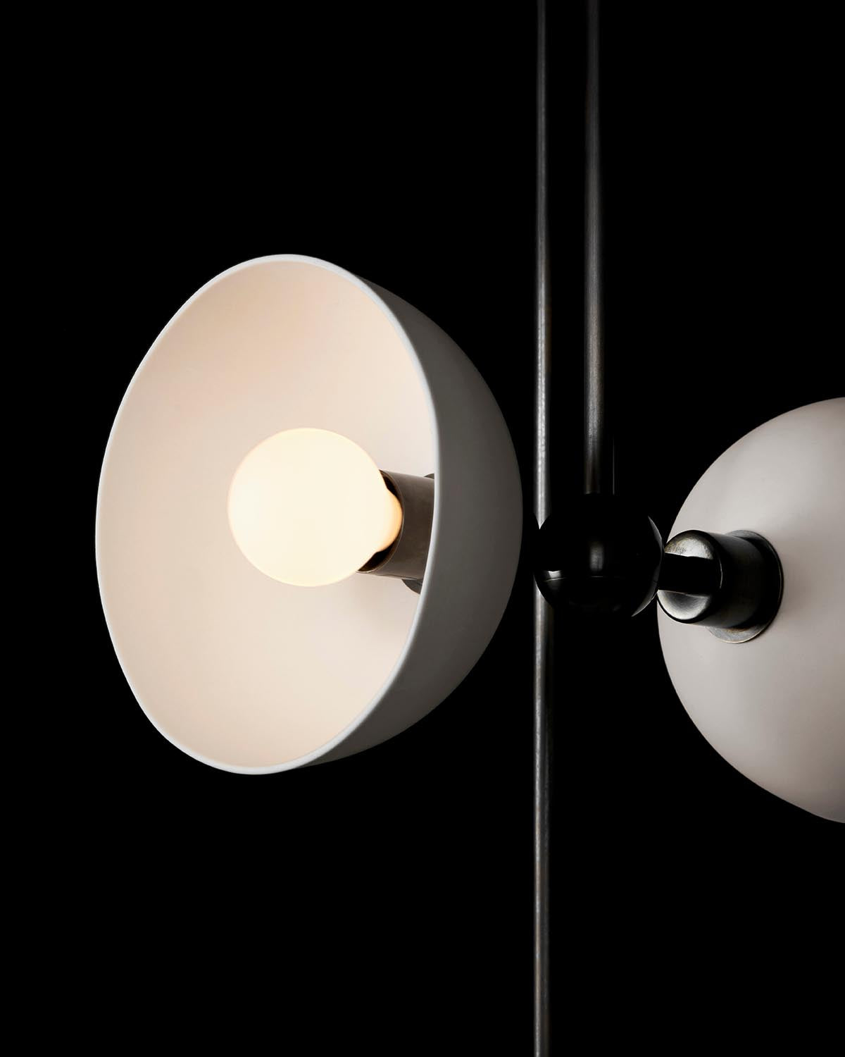 Close-up of modern white metal lampshade with exposed bulb on black metal rod against black background