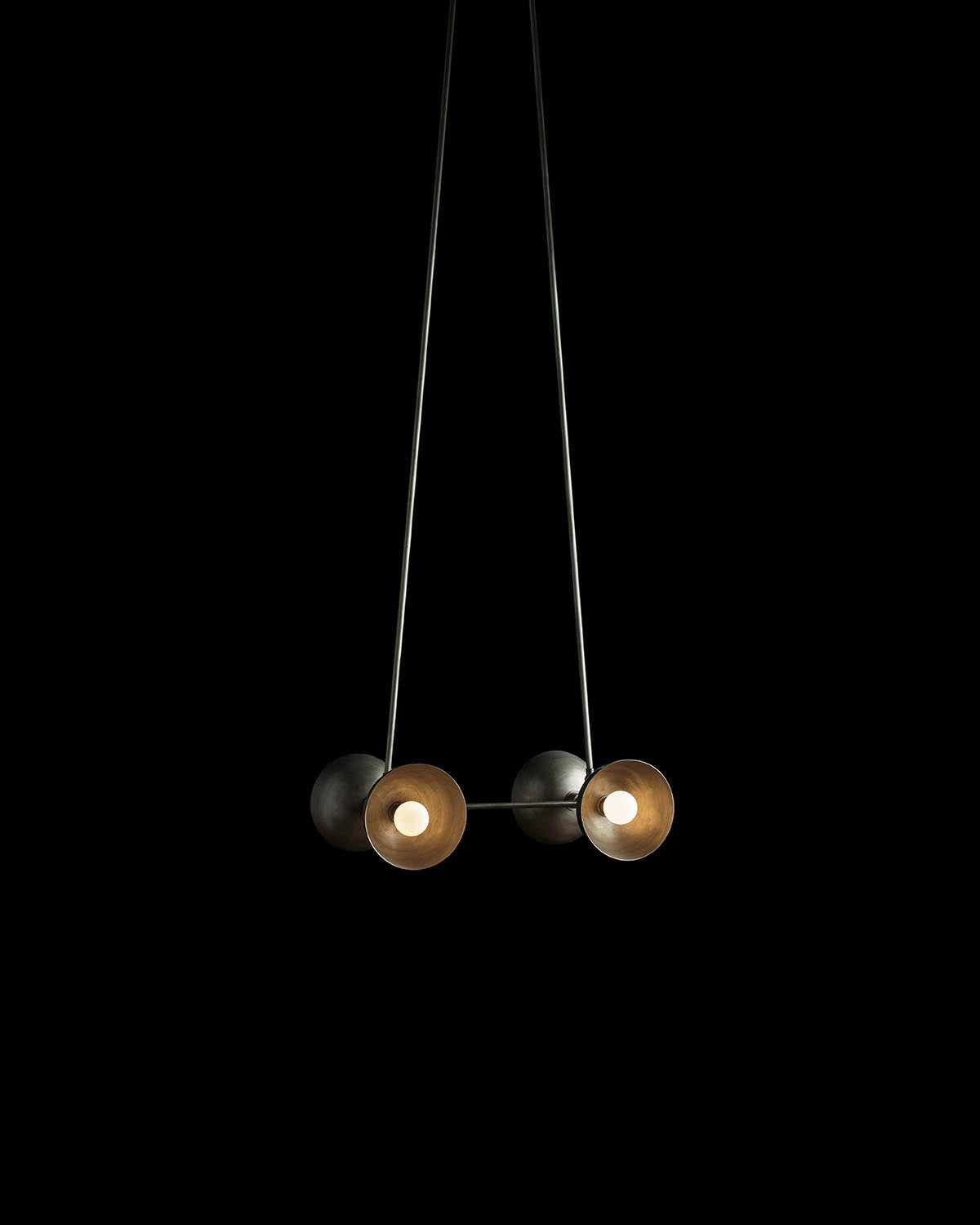 Minimalist four-light pendant fixture with round black and brass shades suspended by thin black rods against a dark background