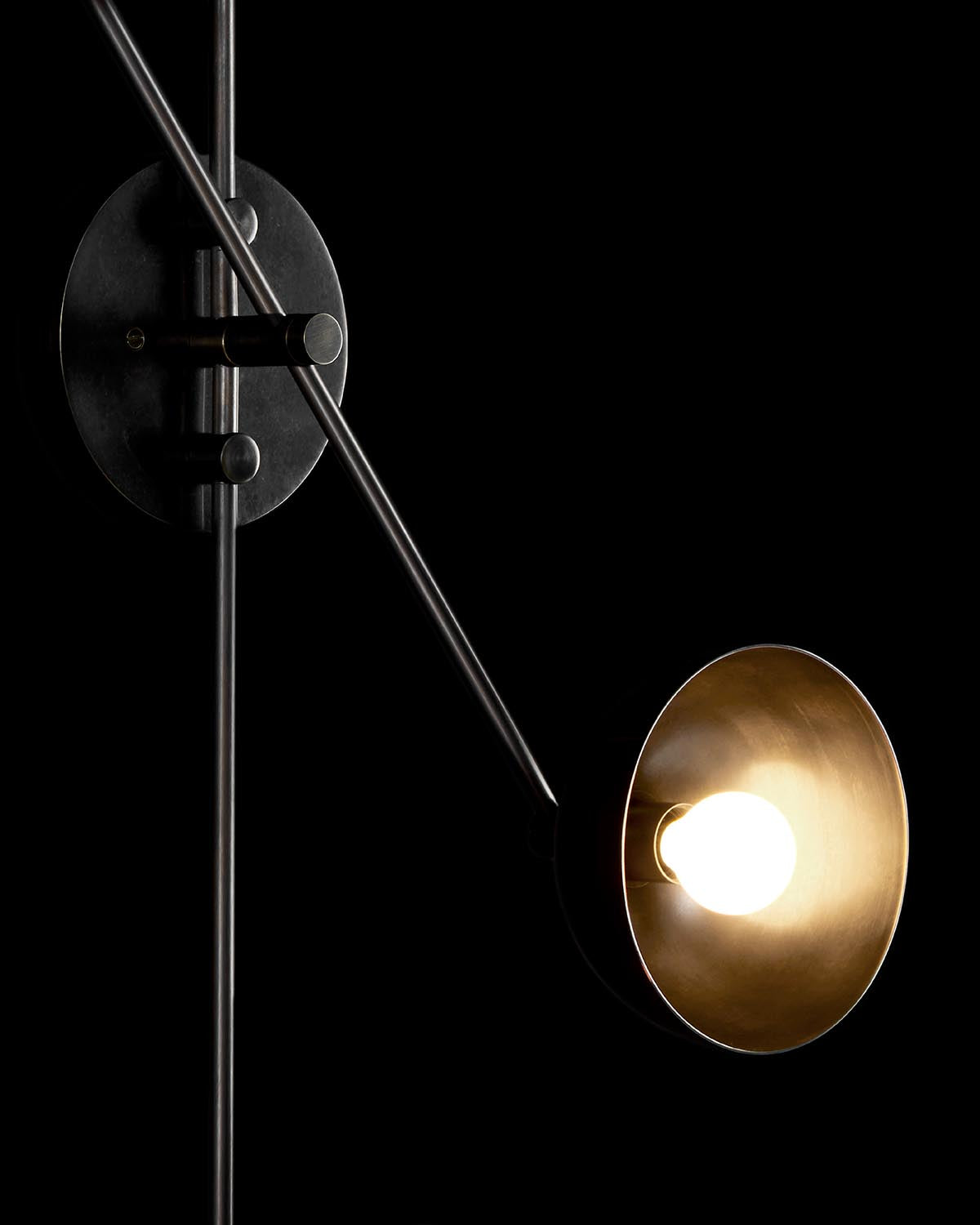 Close-up of modern black metal wall lamp with round shade illuminating a warm light against a dark background