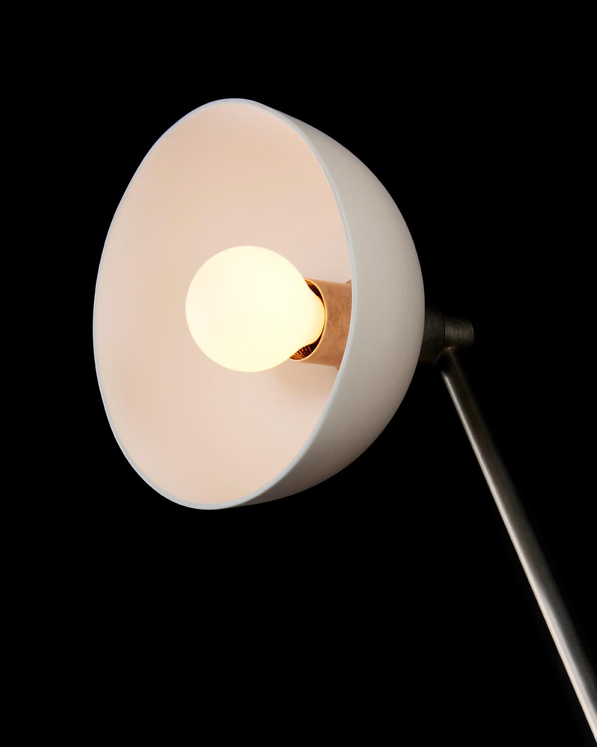 Close-up of a white cone-shaped lamp shade with illuminated bulb, mounted on a slim metallic rod against a black background