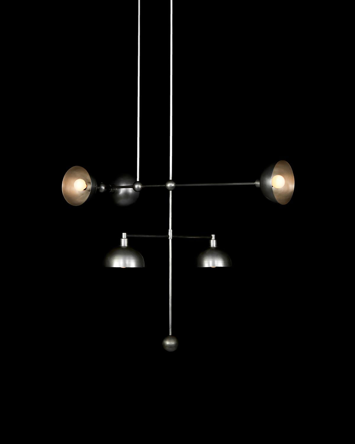 Minimalist suspended lighting fixture with five metal lampshades arranged asymmetrically on thin rods against black background