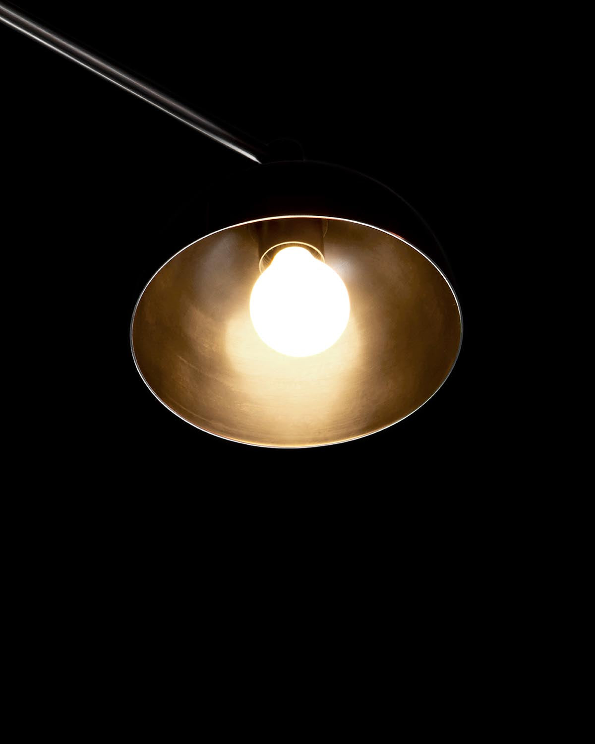 Close-up of a modern pendant light with a glowing bulb inside a smooth metal shade against a black background
