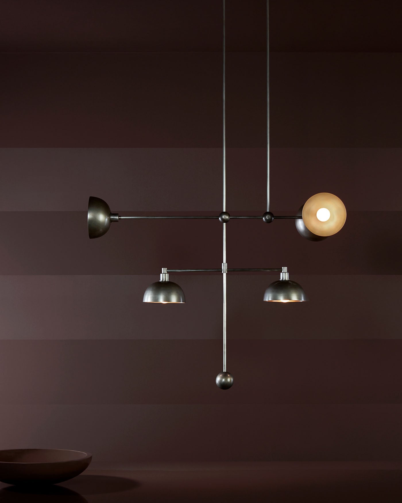 Minimalist metal mobile chandelier with five light fixtures suspended against a dark striped wall background