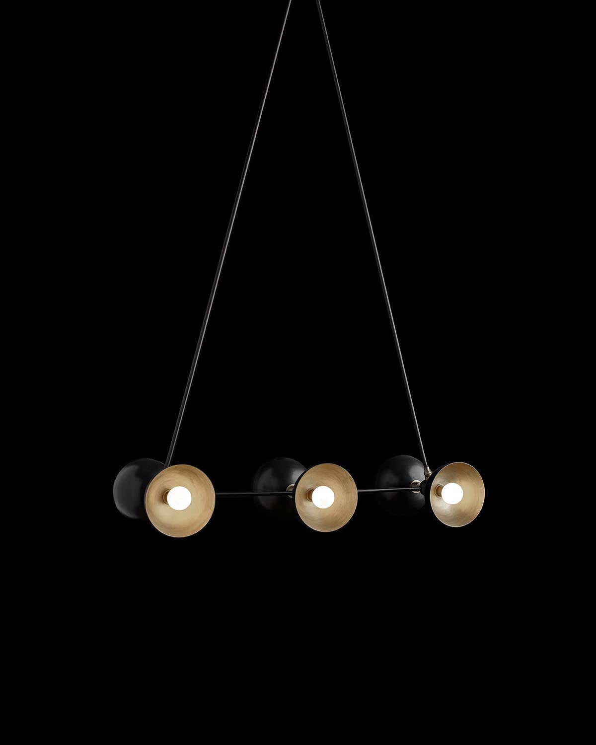 Modern pendant light fixture with six round brass and black shades suspended by thin wires on black background