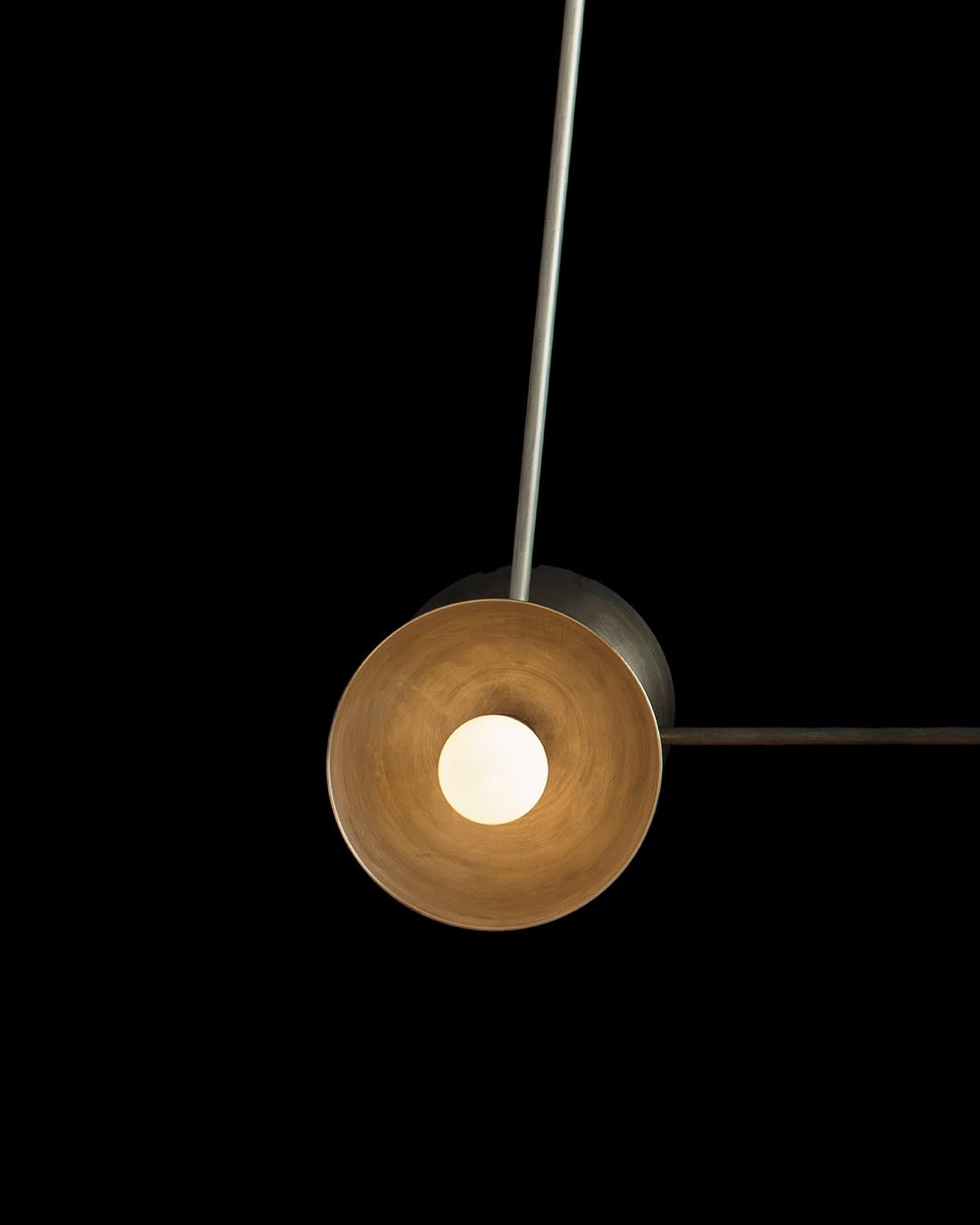 Close-up of a single round pendant light with warm inner surface and exposed bulb against a black background