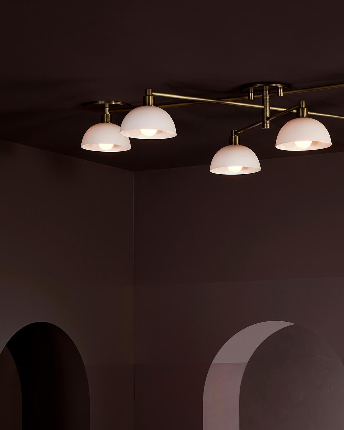 Modern ceiling light fixture with six white dome shades and brass arms against a dark ceiling background