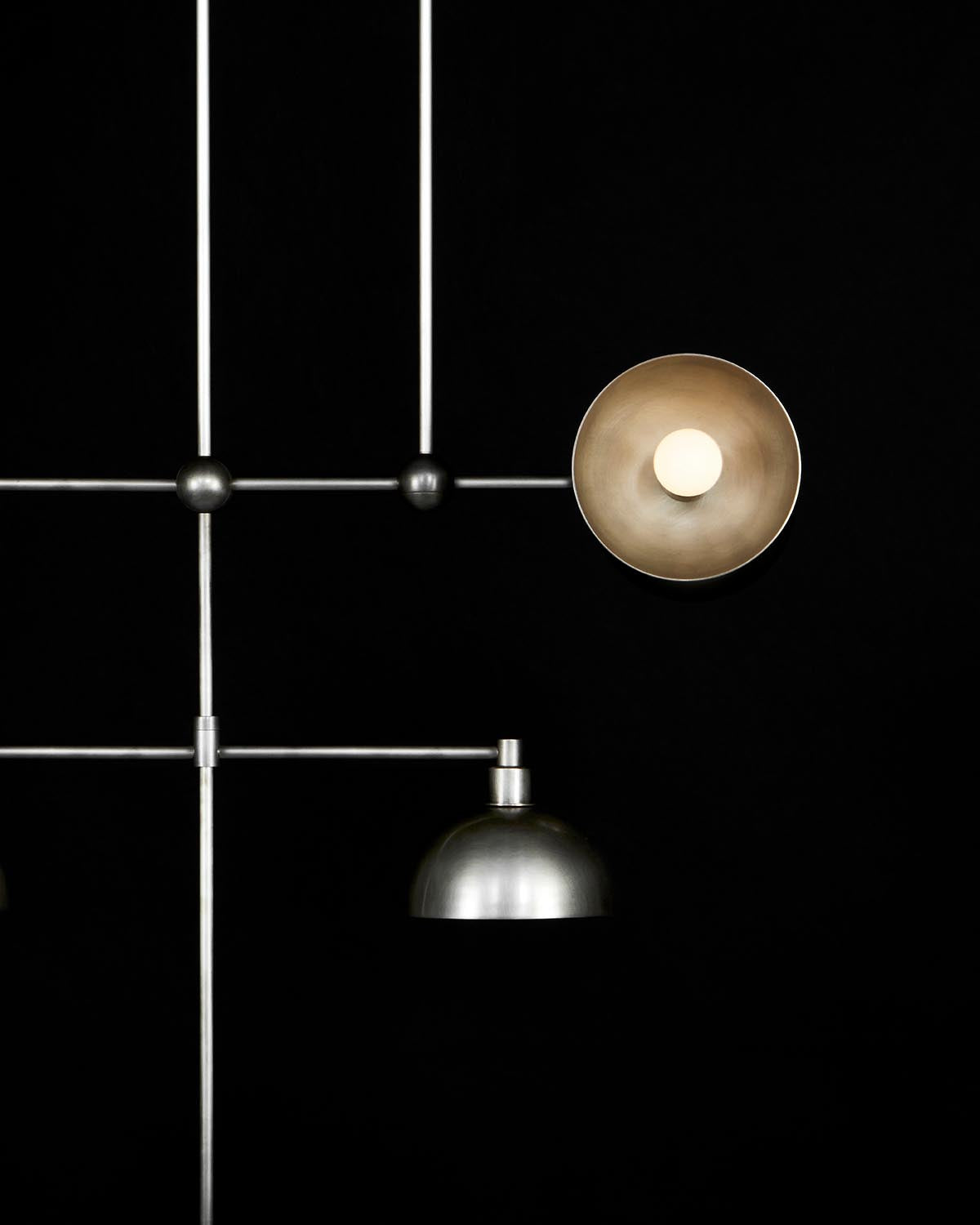 Minimalist metallic mobile with two distinct lampshades suspended on thin rods against a black background