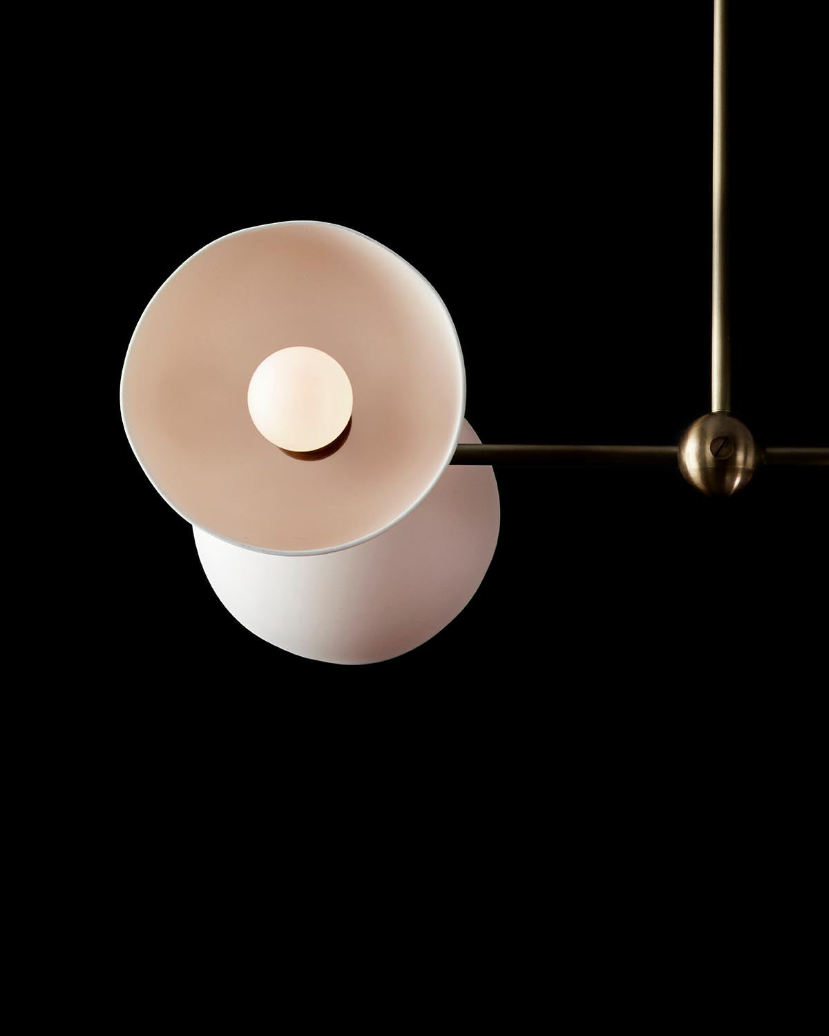 Close-up of a modern pendant light with overlapping circular shades and brass accents against a black background