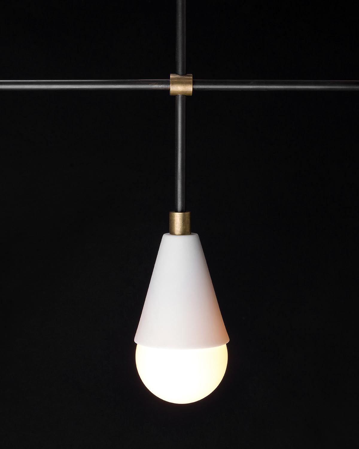 Close-up of a single white conical glass pendant light with glowing bulb hanging from dark metal rod with brass fittings on black background