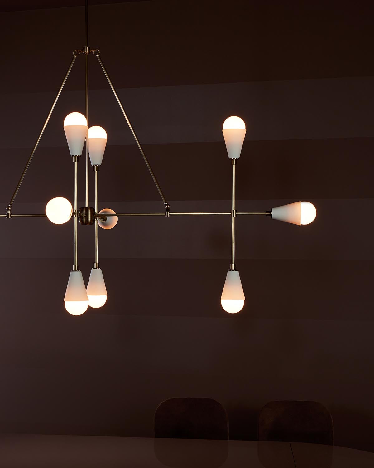 Minimalist linear pendant light fixture with twelve frosted bulb covers suspended in a geometric brass frame against a dark background