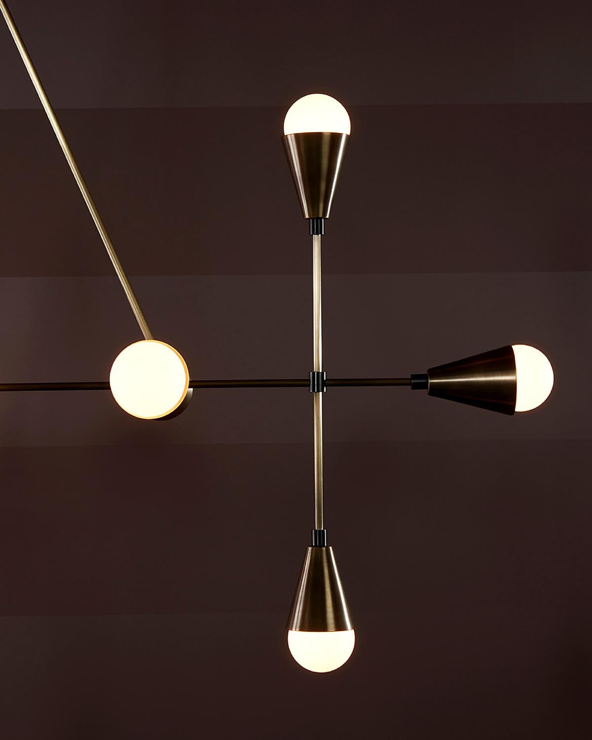 Close-up of modern linear pendant light with four conical brass fixtures and frosted glass bulbs on dark background