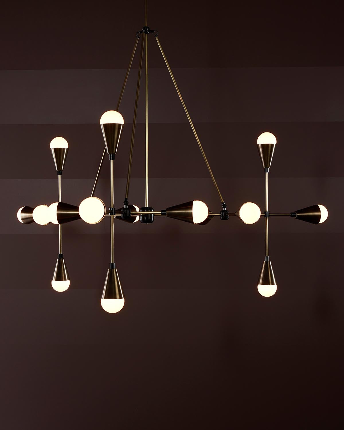 Modern pendant light fixture with multiple cone-shaped bulbs on brass rods against a dark brown background