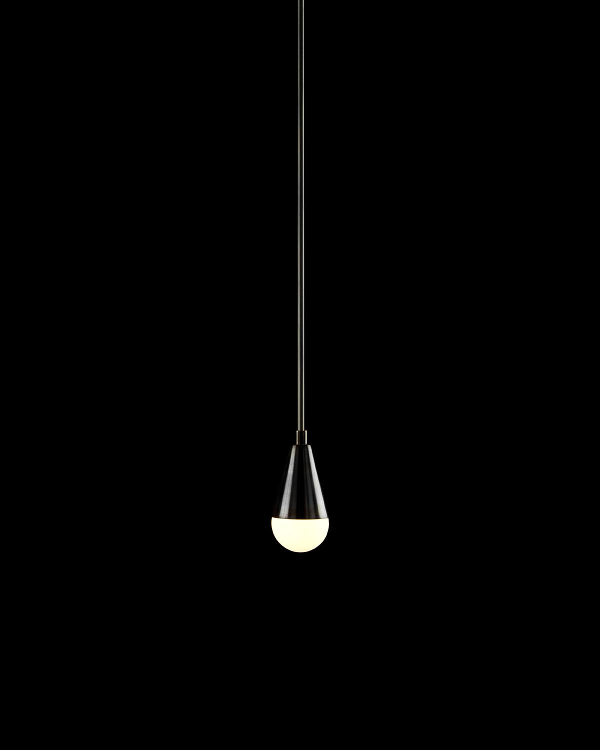 Single minimalist pendant light with black cone shade and round white bulb suspended on a thin black cord against black background