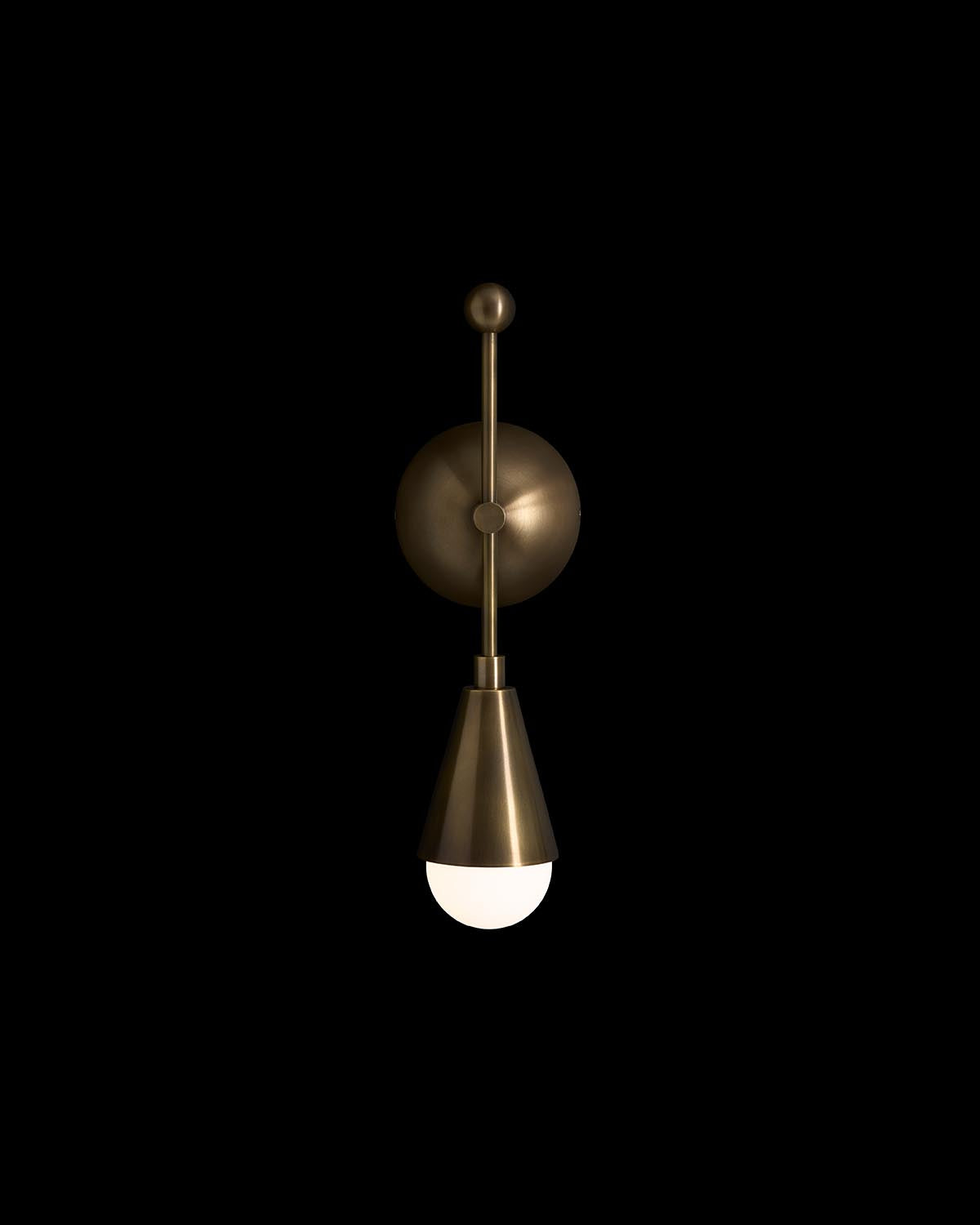 Single modern bronze wall sconce with a cone-shaped shade and round white bulb against a black background