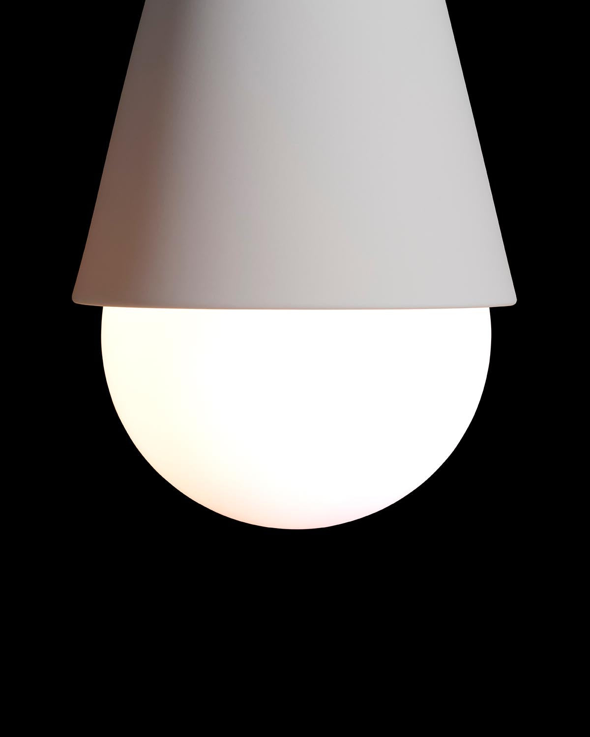 Close-up of a modern white wall sconce with a conical shade and glowing round bulb on a black background