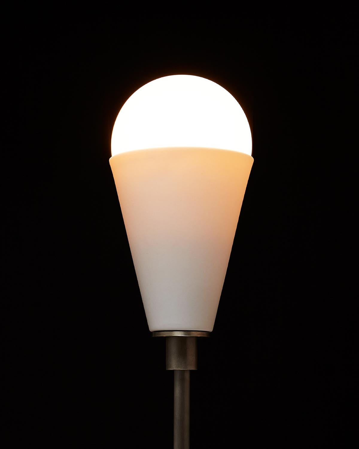 Close-up of a modern wall sconce with a glowing round bulb in a matte white conical shade against a black background