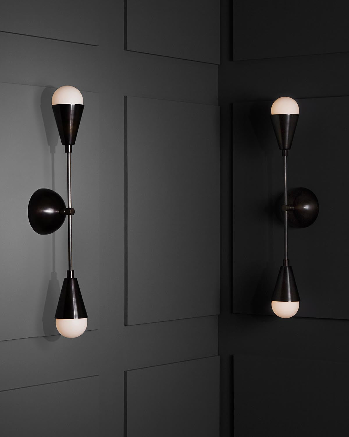 Pair of modern black metal wall sconces with white glass bulb covers mounted on dark paneled walls