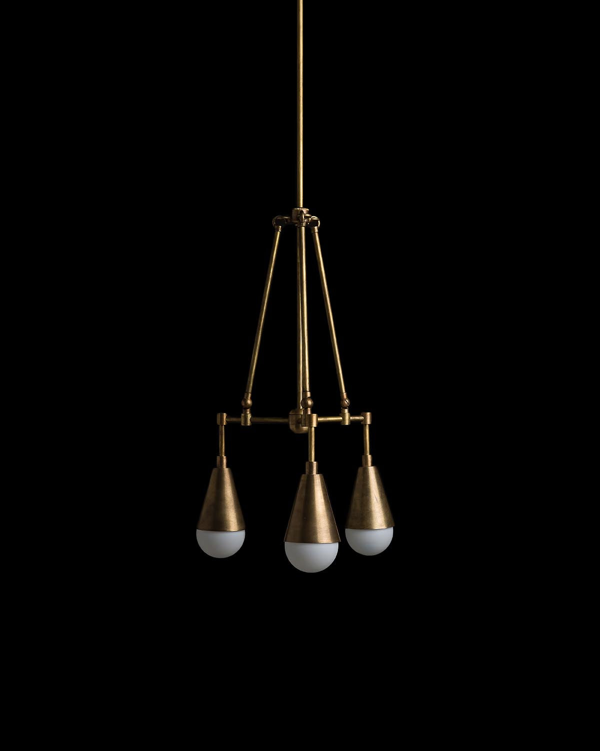 Triangular arrangement of three brass pendant lights with white globes suspended against a black background