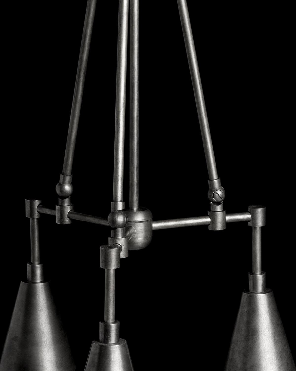 Close-up of three conical metal pendant lights with adjustable arms and joints against a black background