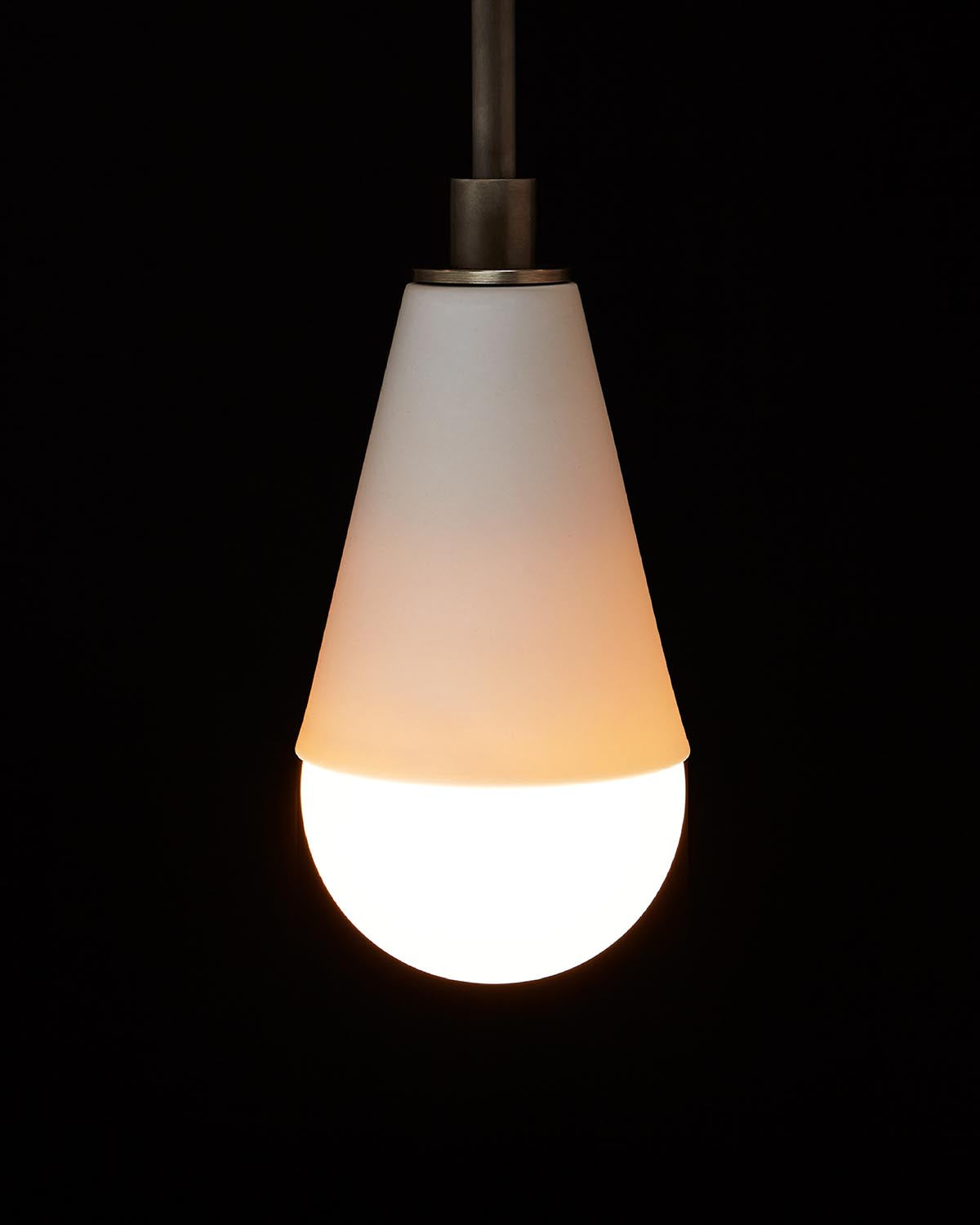 Single cone-shaped pendant light with frosted white shade and glowing bulb against black background