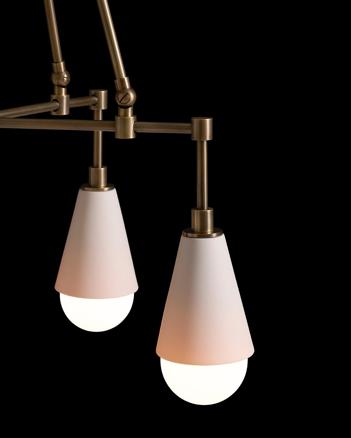 Close-up of two white conical pendant lights with antique brass fittings against a black background