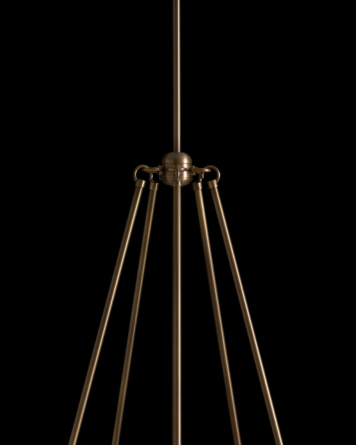 Close-up of modern brass pendant light fixture with five elongated arms against a black background