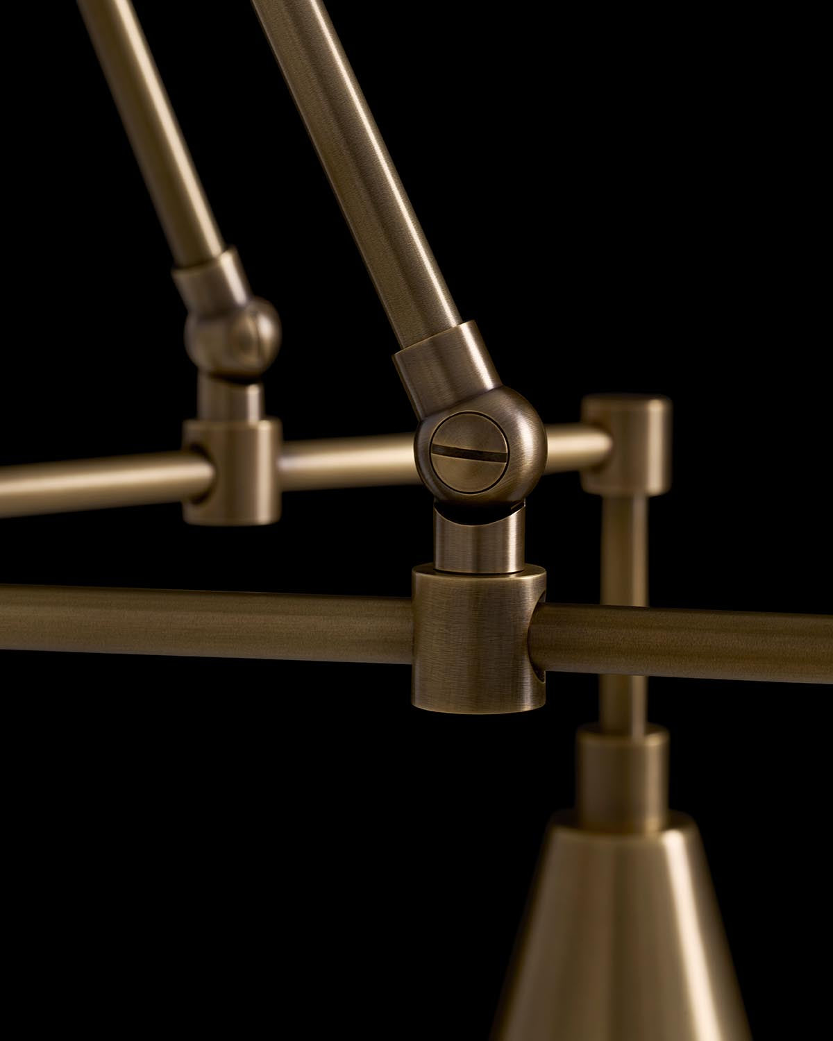 Close-up of bronze metal joints and rods forming part of a modern pendant light against a black background