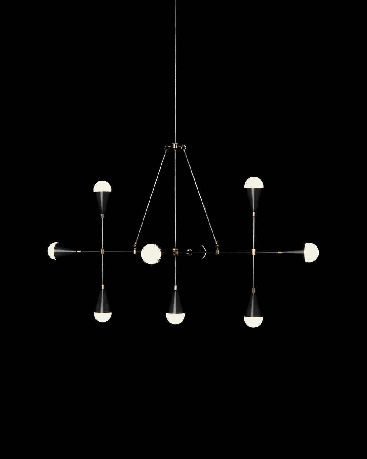 Minimalist black and brass linear pendant light with nine white half-sphere bulbs suspended on cords against black background