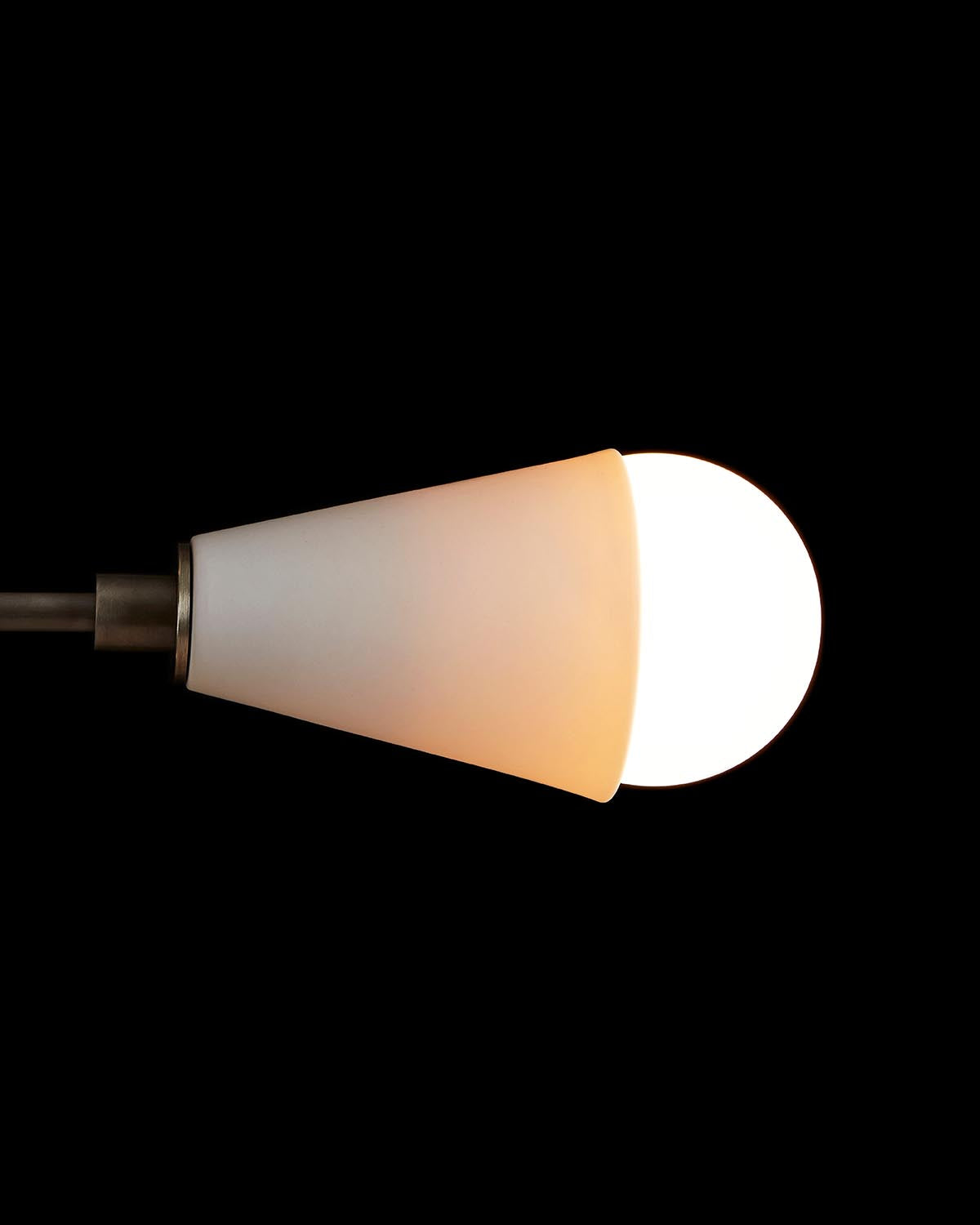Close-up of a conical frosted glass pendant light with exposed glowing bulb on a dark background