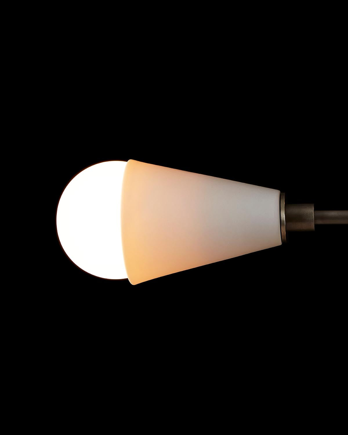 Close-up of a conical frosted glass pendant light with exposed glowing bulb on a dark background