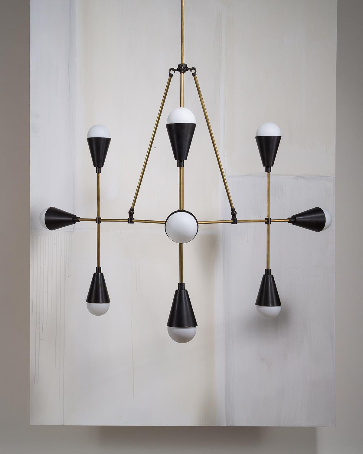 Geometric pendant light fixture with nine black cone-shaped shades and brass rods against a neutral wall background