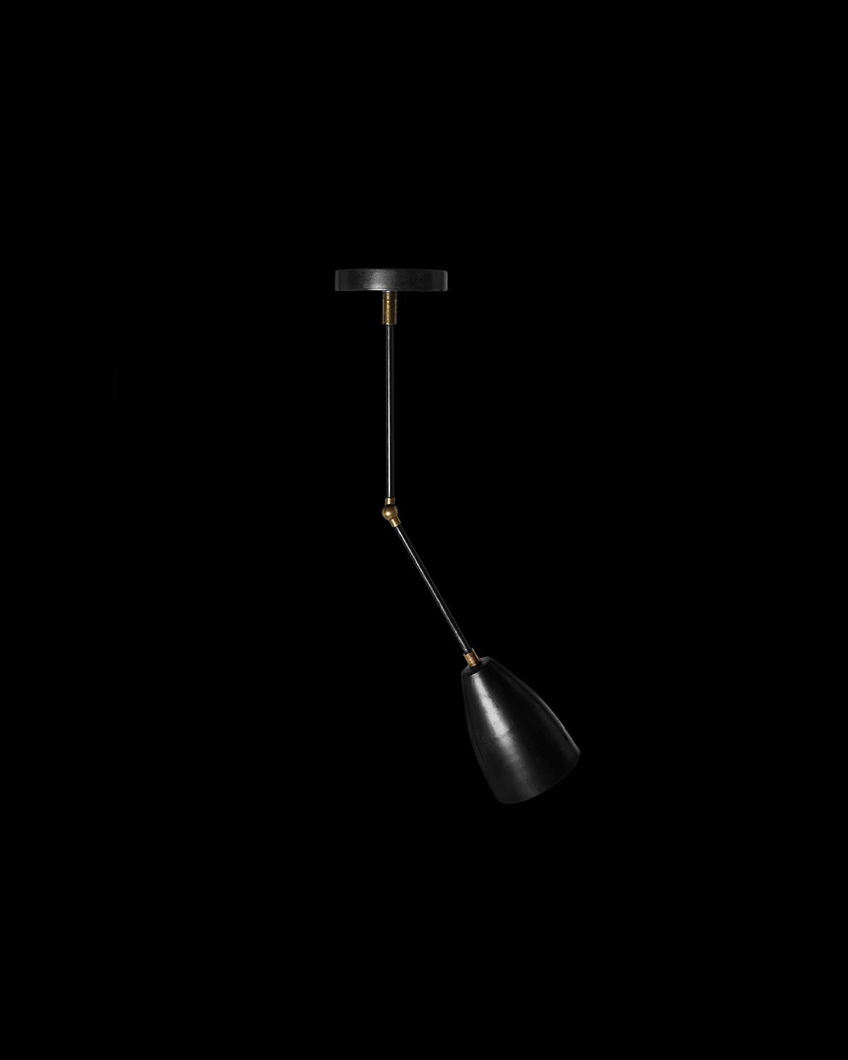 Minimalist black downlight with angled adjustable arm and brass accents against a black background