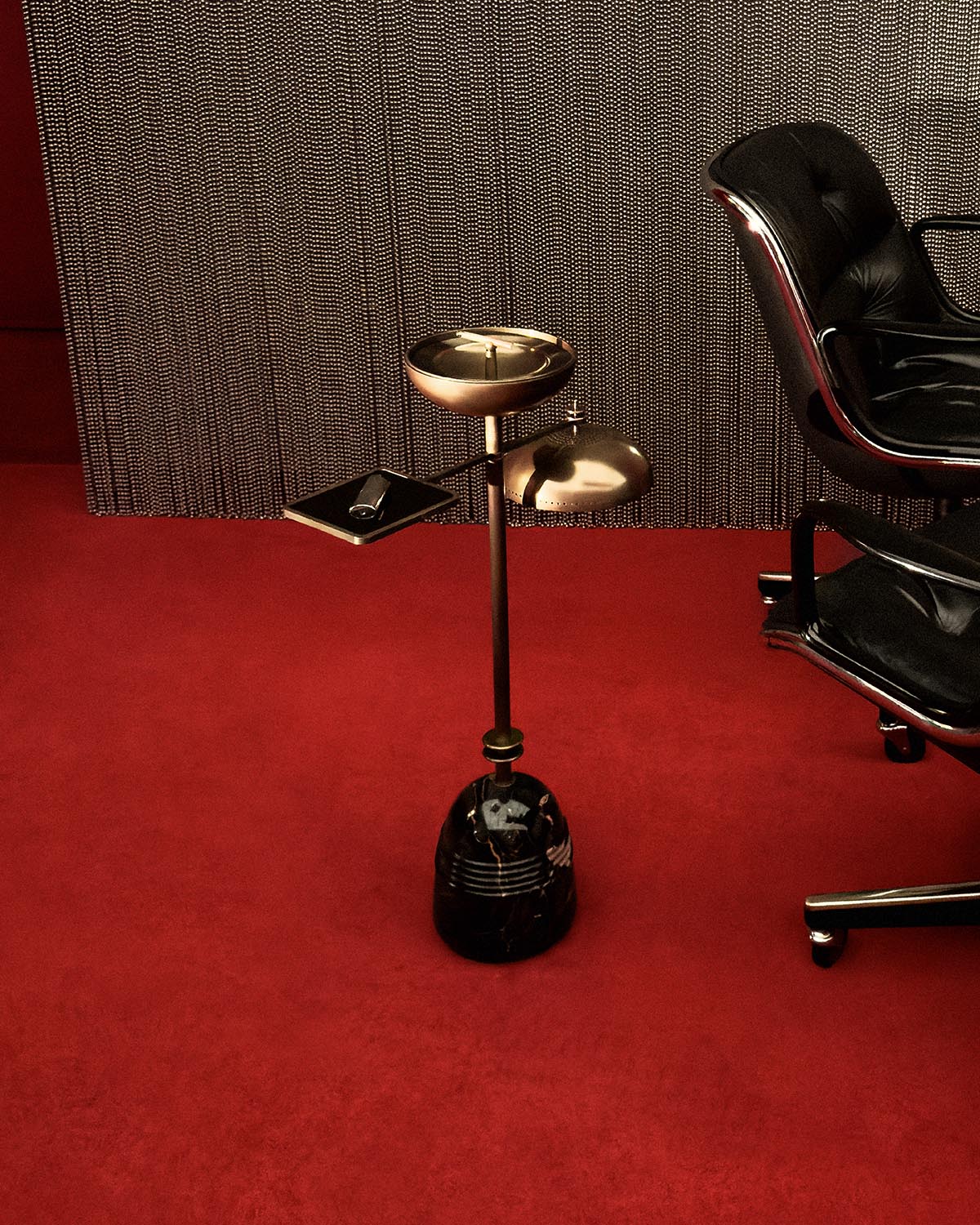 Modern smoking table with brass trays and black base, positioned on red carpet next to black leather office chair
