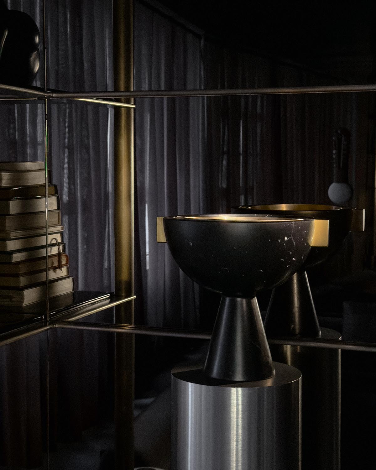 Black marble vessel with conical base and gold accents displayed on a metallic pedestal against reflective surfaces