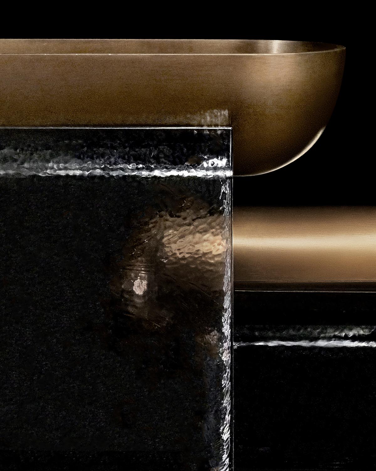 Close-up of a minimalist bronze vessel resting on a textured black stone block against a dark background