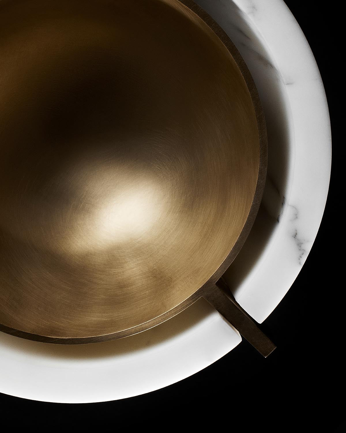 Top view of a metallic bronze vessel nested inside a round white marble bowl with veined texture on a black background